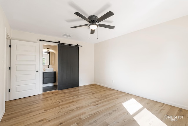 unfurnished bedroom featuring connected bathroom, ceiling fan, light hardwood / wood-style flooring, and a barn door