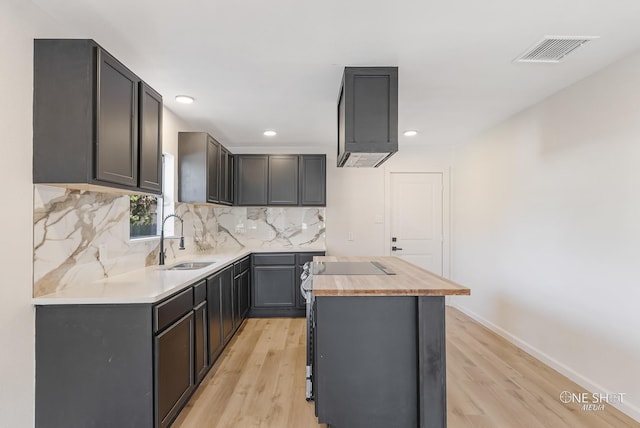 kitchen with decorative backsplash, light hardwood / wood-style floors, black electric stovetop, sink, and butcher block countertops