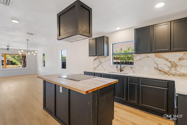 kitchen featuring decorative backsplash, butcher block counters, black electric cooktop, light hardwood / wood-style flooring, and an inviting chandelier