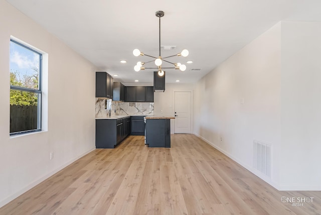 kitchen with tasteful backsplash, hanging light fixtures, sink, light hardwood / wood-style floors, and a center island