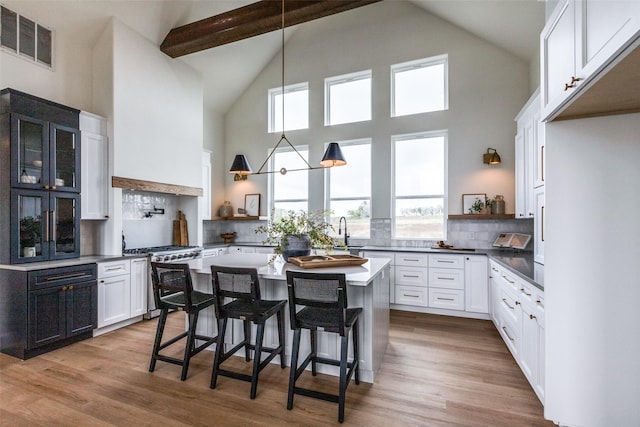 kitchen with high end range, white cabinetry, tasteful backsplash, light hardwood / wood-style floors, and a breakfast bar