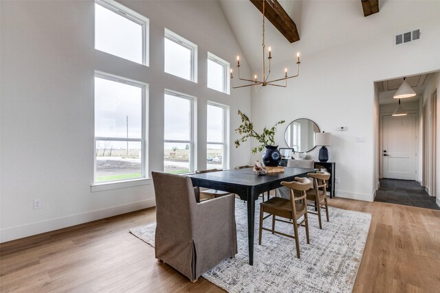 dining space with a towering ceiling, hardwood / wood-style floors, beamed ceiling, and a chandelier