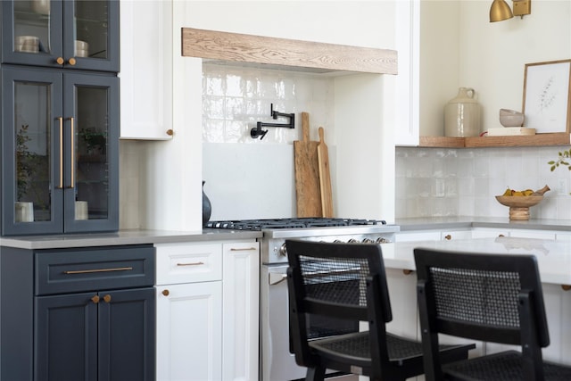 kitchen with white cabinetry, blue cabinetry, stainless steel stove, and backsplash