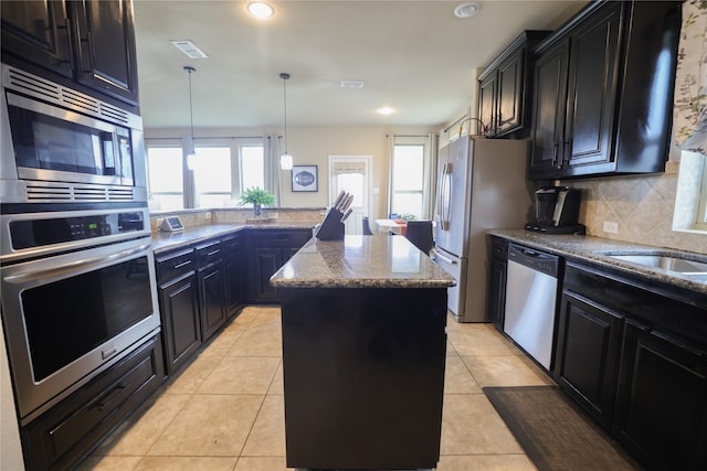 kitchen featuring hanging light fixtures, backsplash, appliances with stainless steel finishes, a kitchen island, and light stone counters