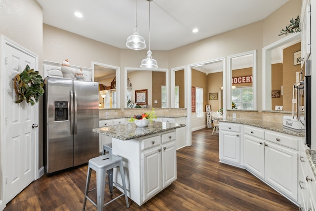 kitchen with stainless steel refrigerator with ice dispenser, white cabinetry, dark hardwood / wood-style flooring, a kitchen island, and pendant lighting