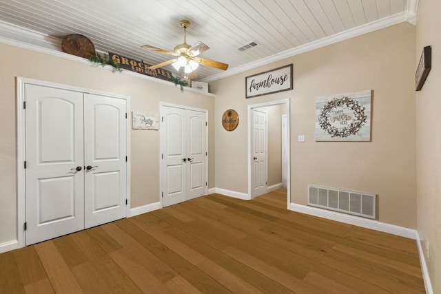 unfurnished bedroom featuring crown molding, ceiling fan, wood-type flooring, and multiple closets