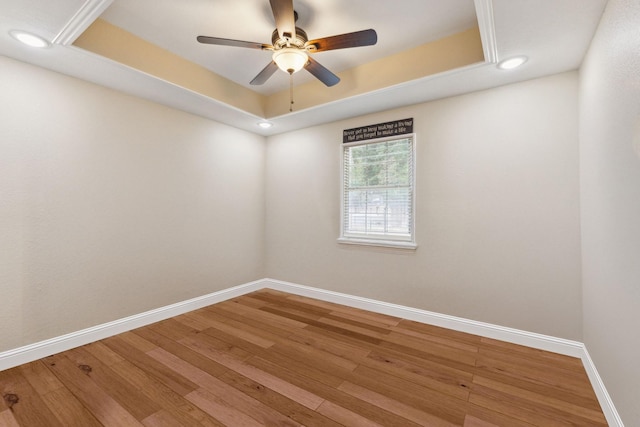 unfurnished room featuring a raised ceiling, wood-type flooring, and ceiling fan