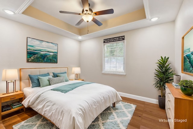 bedroom featuring a tray ceiling, ceiling fan, and light wood-type flooring