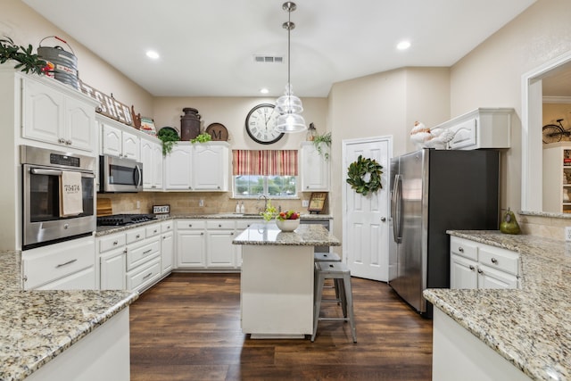 kitchen featuring stainless steel appliances, a center island, decorative backsplash, white cabinets, and decorative light fixtures