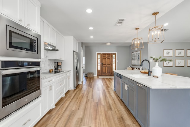 kitchen featuring a large island with sink, stainless steel appliances, hanging light fixtures, and white cabinets