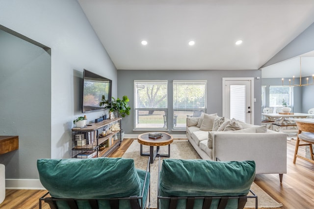 living room with light hardwood / wood-style floors, a notable chandelier, lofted ceiling, and plenty of natural light