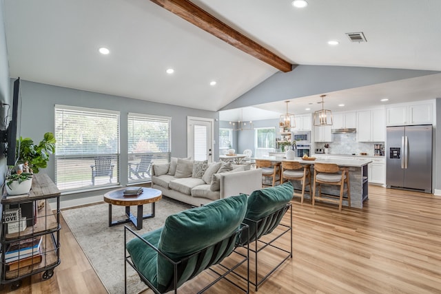 living room featuring a notable chandelier, light hardwood / wood-style floors, a healthy amount of sunlight, and vaulted ceiling with beams