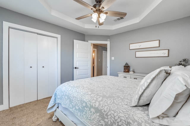 carpeted bedroom featuring a closet, ceiling fan, and a tray ceiling