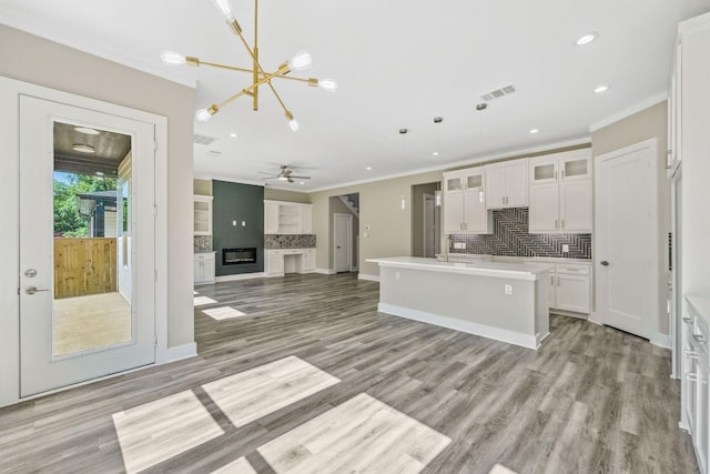 kitchen featuring white cabinets, tasteful backsplash, hanging light fixtures, an island with sink, and light hardwood / wood-style floors