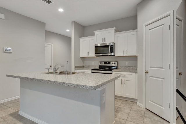 kitchen with an island with sink, stainless steel appliances, sink, light tile patterned floors, and white cabinetry