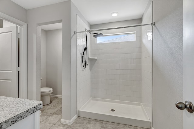 bathroom with vanity, a tile shower, toilet, and tile patterned flooring