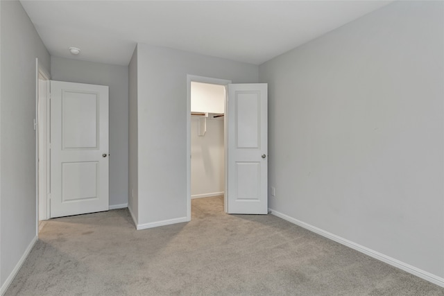 unfurnished bedroom with a closet, light carpet, and a spacious closet