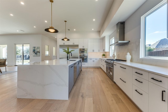 kitchen with wall chimney range hood, hanging light fixtures, appliances with stainless steel finishes, a large island, and white cabinetry