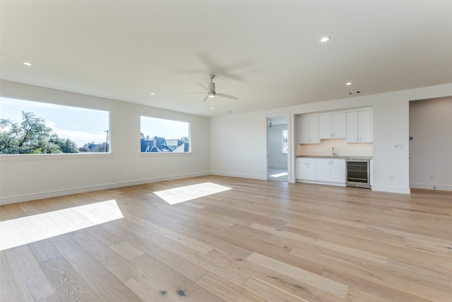 unfurnished living room featuring ceiling fan, light hardwood / wood-style floors, and wine cooler