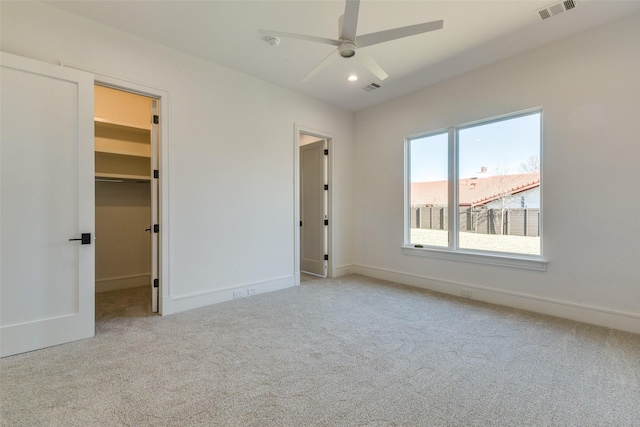 unfurnished bedroom with a walk in closet, ceiling fan, a closet, and light carpet