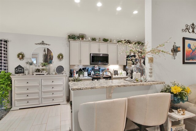 kitchen featuring decorative backsplash, kitchen peninsula, a breakfast bar, white cabinetry, and appliances with stainless steel finishes