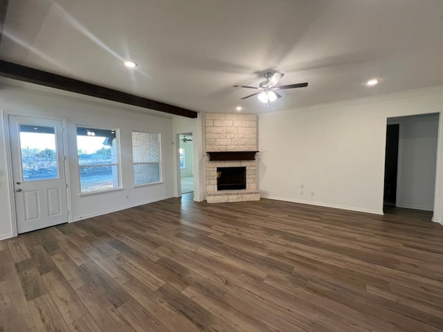 unfurnished living room with ceiling fan, beam ceiling, crown molding, dark wood-type flooring, and a stone fireplace