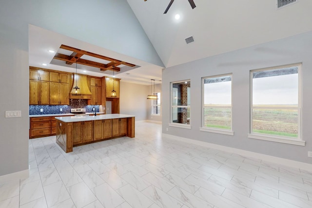 kitchen with hanging light fixtures, tasteful backsplash, custom exhaust hood, a kitchen island with sink, and electric range