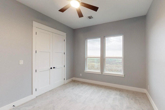 unfurnished bedroom with a closet, light colored carpet, and ceiling fan