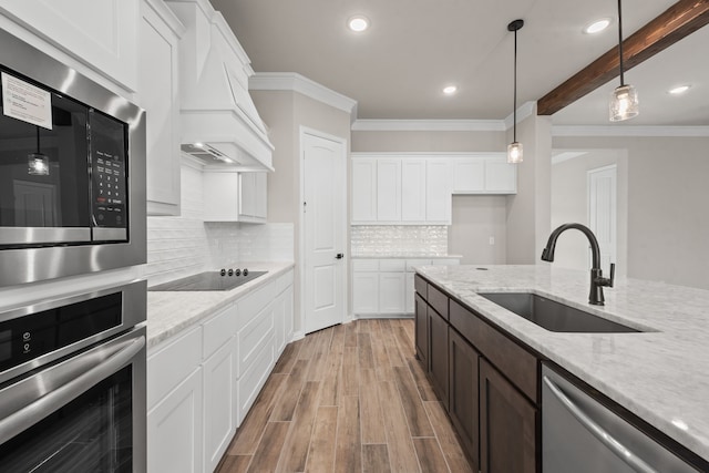 kitchen featuring light wood-type flooring, stainless steel appliances, custom exhaust hood, white cabinetry, and a sink