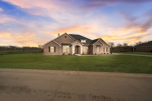 french country style house featuring brick siding, a chimney, and a front yard