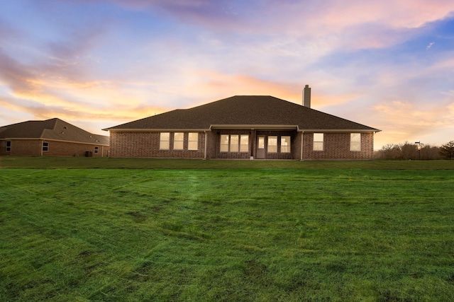 back of property at dusk with a yard, brick siding, and a chimney