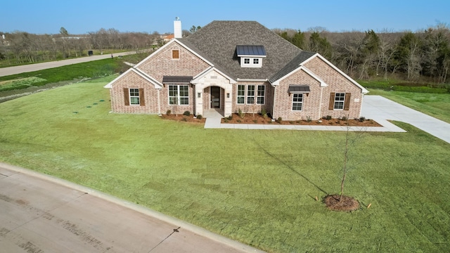 view of front of home with brick siding, a chimney, a front lawn, and roof with shingles