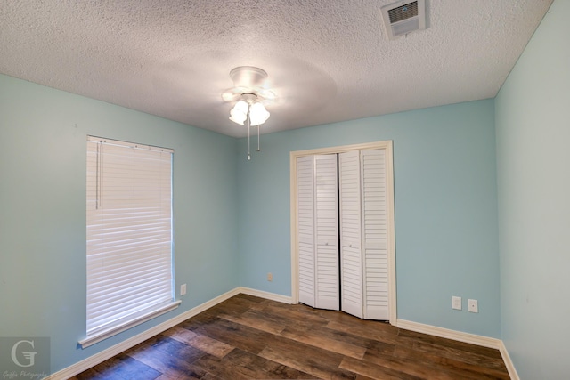 unfurnished bedroom with dark wood-style flooring, a closet, visible vents, and baseboards