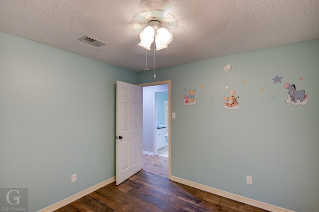 empty room featuring baseboards, a textured ceiling, visible vents, and dark wood-type flooring