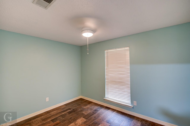 empty room with a textured ceiling, dark wood-type flooring, visible vents, and baseboards