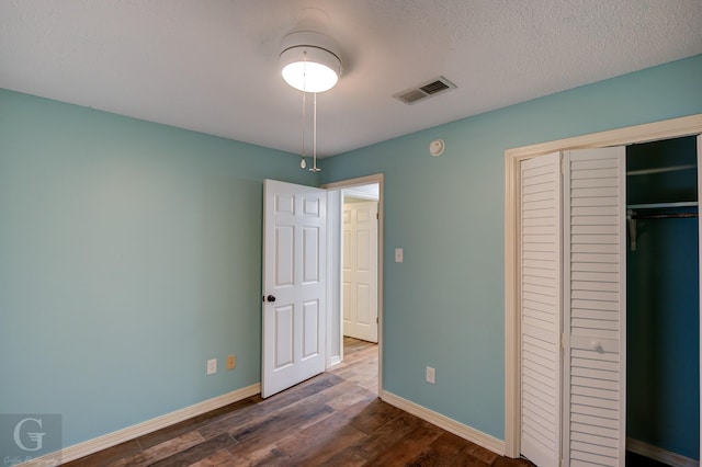 unfurnished bedroom featuring baseboards, a textured ceiling, visible vents, and dark wood-type flooring