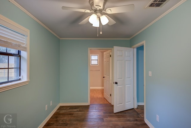 empty room featuring a healthy amount of sunlight, crown molding, visible vents, and dark wood-style flooring