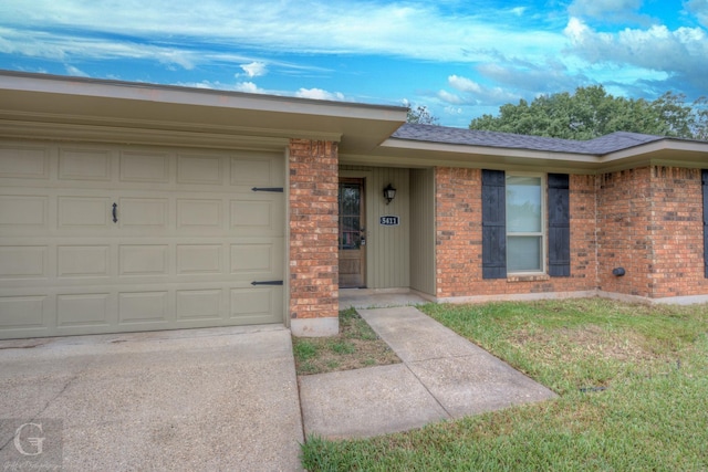 single story home featuring driveway, brick siding, a front lawn, and an attached garage