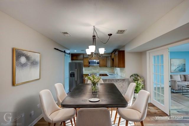 dining space featuring a chandelier, a barn door, wood finished floors, and visible vents