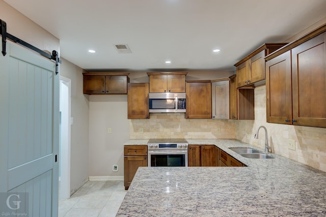 kitchen with a barn door, a sink, visible vents, appliances with stainless steel finishes, and backsplash