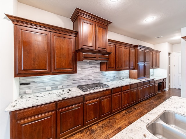 kitchen featuring light stone countertops, dark hardwood / wood-style flooring, tasteful backsplash, a textured ceiling, and stainless steel gas cooktop