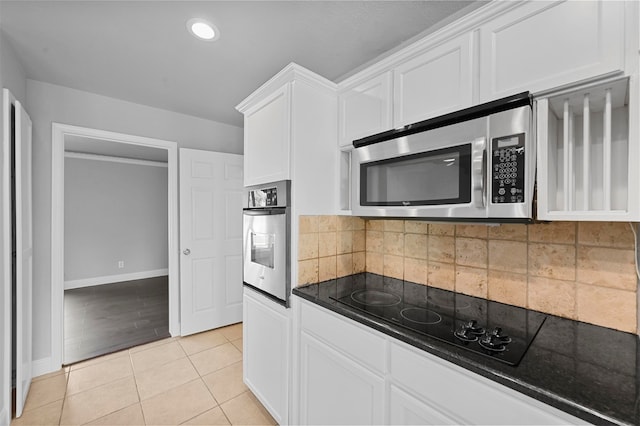 kitchen featuring decorative backsplash, white cabinets, light tile patterned floors, appliances with stainless steel finishes, and dark stone countertops