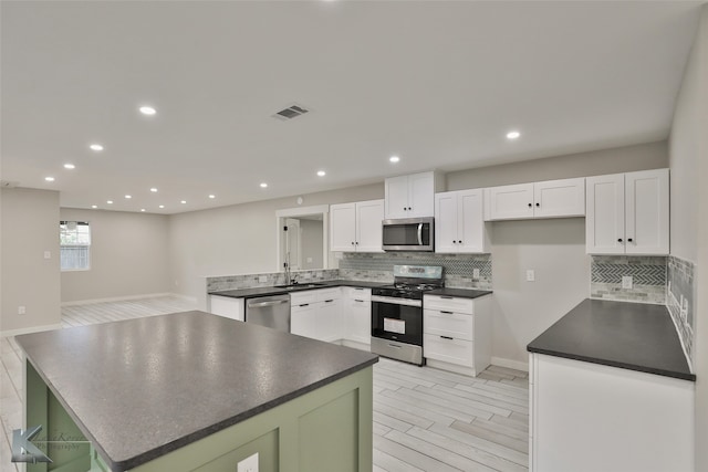 kitchen with decorative backsplash, appliances with stainless steel finishes, white cabinetry, and light hardwood / wood-style floors