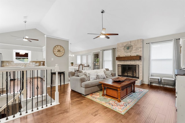 living room featuring a wealth of natural light, a fireplace, wood-type flooring, and ceiling fan with notable chandelier