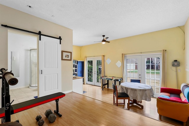 workout area with french doors, ceiling fan, light hardwood / wood-style flooring, and a barn door