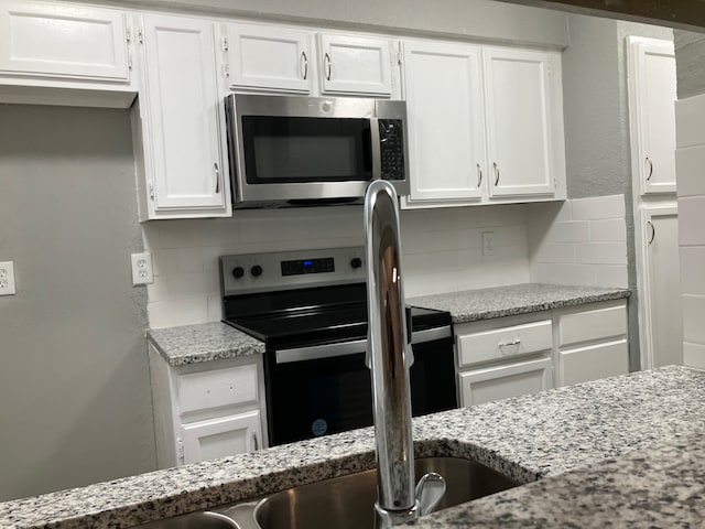 kitchen featuring white cabinetry, light stone countertops, tasteful backsplash, and appliances with stainless steel finishes