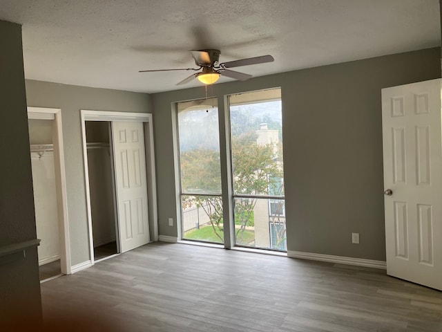 unfurnished bedroom featuring light hardwood / wood-style flooring, two closets, a textured ceiling, and ceiling fan