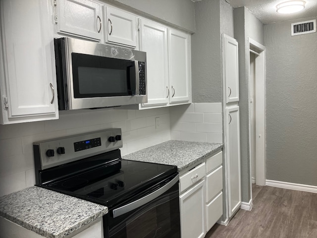 kitchen with decorative backsplash, wood-type flooring, light stone countertops, white cabinetry, and appliances with stainless steel finishes