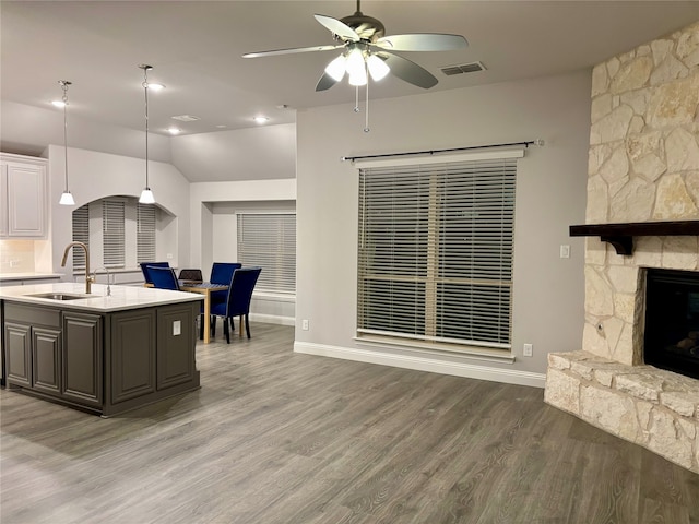 kitchen featuring a stone fireplace, sink, hardwood / wood-style flooring, an island with sink, and decorative light fixtures