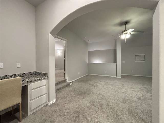 unfurnished living room featuring built in desk, light colored carpet, and ceiling fan